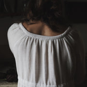 Back view of The Lydia cotton-bamboo dress showing gathered scoop neckline and textured fabric, dim Tuscan interior