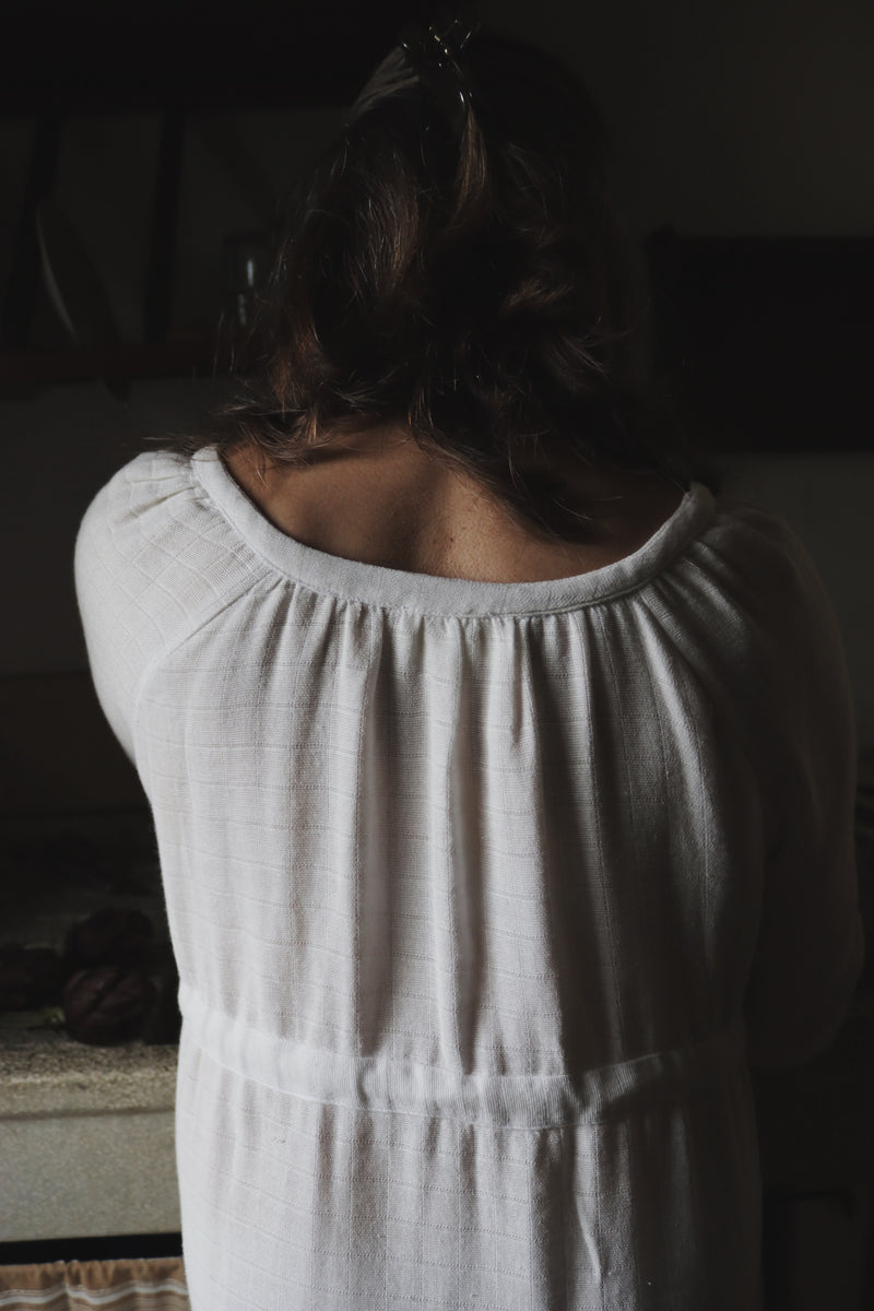 Back view of The Lydia cotton-bamboo dress showing gathered scoop neckline and textured fabric, dim Tuscan interior