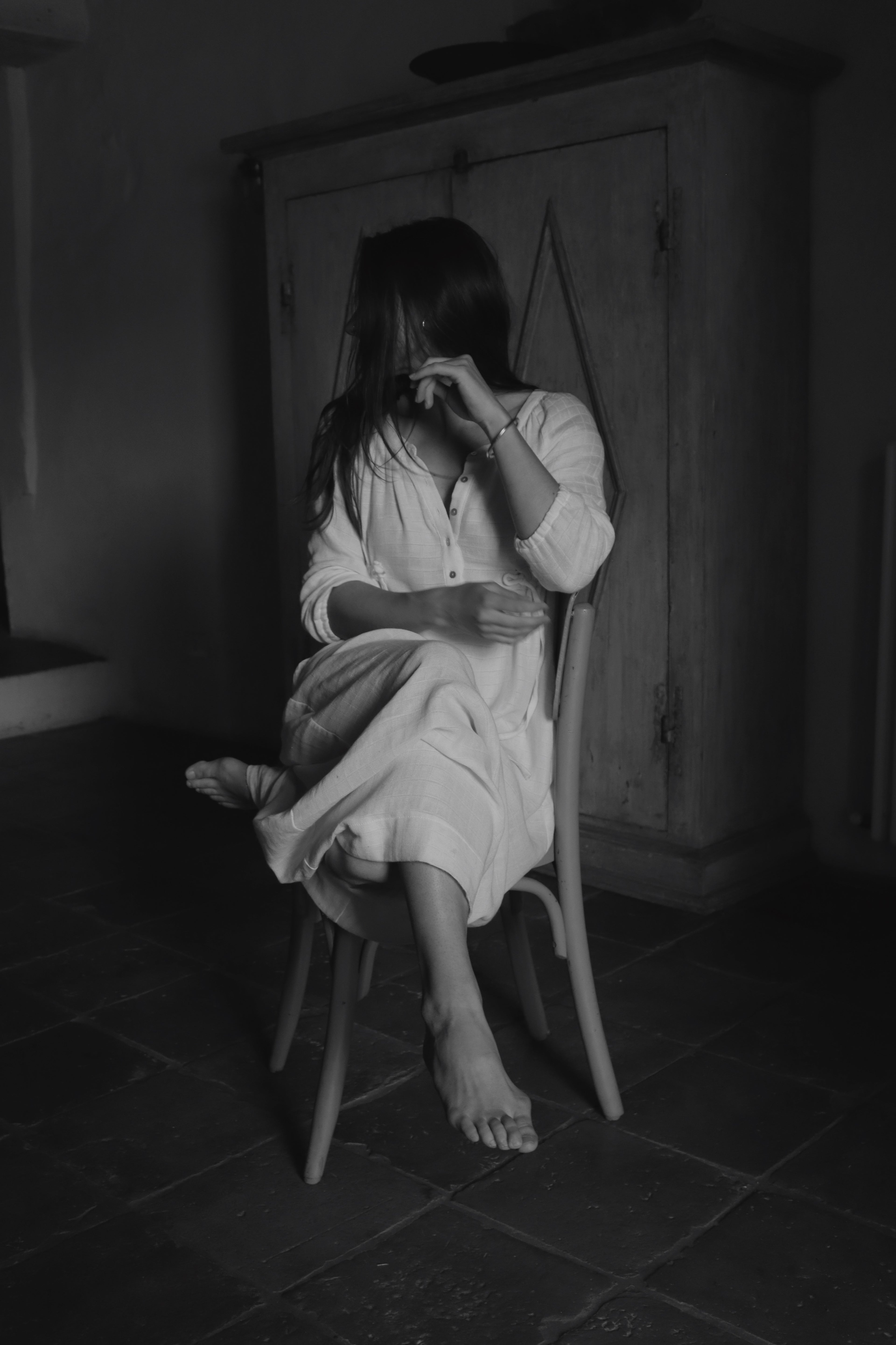 Woman seated in a wooden chair wearing The Lydia cotton-bamboo dress, black and white editorial, Tuscan interior