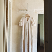 The Thelma cotton dress in cream hanging on an iron hook against a plastered Tuscan wall, full length view