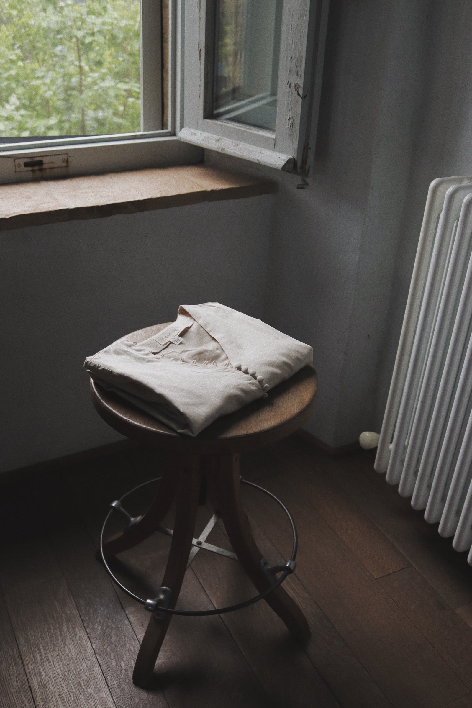 The Thelma folded on a worn wooden stool beside an open window, natural light, old European interior